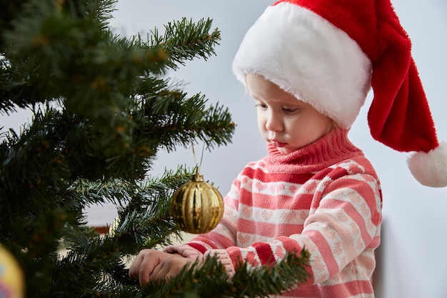 Meisje met kerstmuts hangt een kerstbal aan een kerstboom
