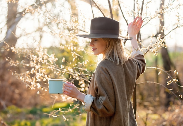 Meisje met kop van koffie in een tuin van de kersenbloesem bij zonsondergang