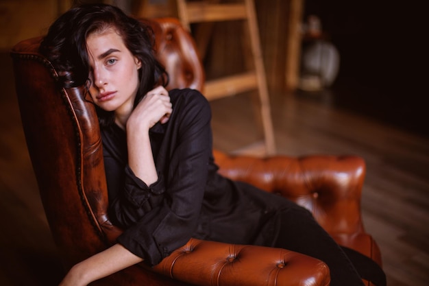 Meisje met krullend donker haar en natuurlijke make-up zittend op een leren stoel vintage fotoverwerking