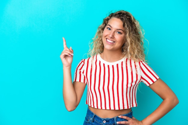 Meisje met krullend haar geïsoleerd op een blauwe achtergrond die een vinger toont en optilt in teken van de beste