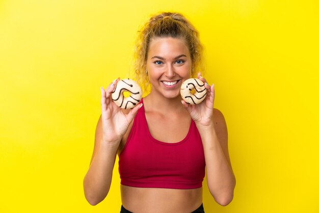 Meisje met krullend haar geïsoleerd op gele achtergrond met donuts met gelukkige uitdrukking