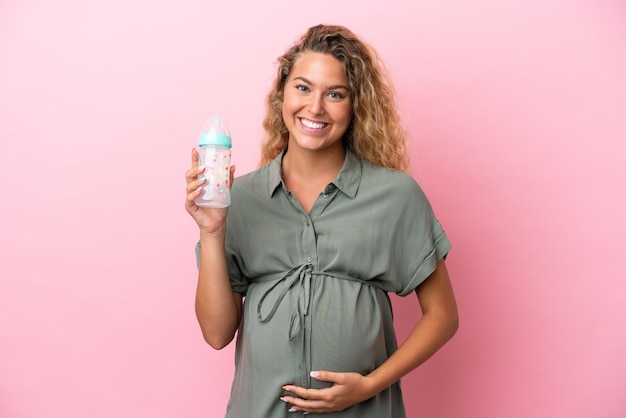 Meisje met krullend haar geïsoleerd op roze achtergrond zwanger en met een zuigfles