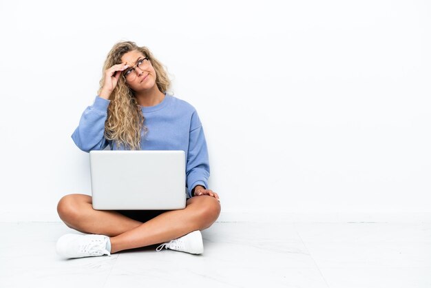 Meisje met krullend haar met een laptop die op de grond zit met twijfels en met een verwarde gezichtsuitdrukking