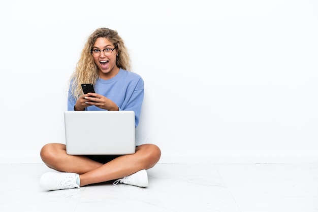 Meisje met krullend haar met een laptop die verrast op de grond zit en een bericht stuurt