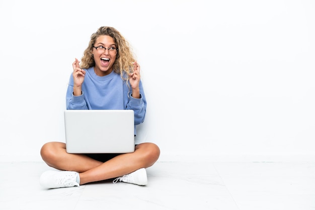 Meisje met krullend haar met een laptop zittend op de vloer met gekruiste vingers