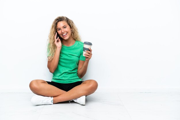 Meisje met krullend haar zittend op de vloer met koffie om mee te nemen en een mobiel