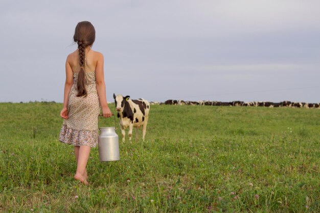 Meisje met lang donker haar en retro blikje in de hand gaat naar de koe op de weide voor melk