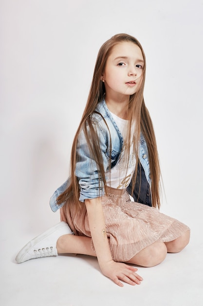 Meisje met lang haar vliegen in de wind en in een spijkerjasje poseren op een lichtroze achtergrond. Jong model, opleiding, foto poseren