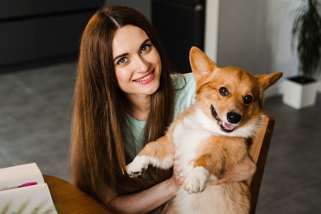 Meisje met laptop glimlacht en speelt thuis met Corgi-hond Programmeurvrouw die online werkt en een pauze heeft om haar hond te knuffelen Plezier hebben met Welsh Corgi Pembroke