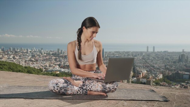 Meisje met laptop in de stad Barcelona Yoga vrouw zittend in lotus houding op de mat