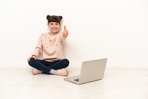 Meisje met laptop zittend op de vloer met duimen omhoog omdat er iets goeds is gebeurd