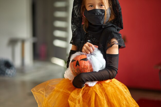 Meisje met masker thuis in halloween kostuum met pompoen Jack of Laurent