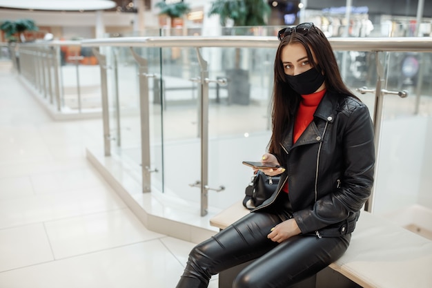 Meisje met medisch zwart masker en mobiele telefoon in een winkelcentrum. .