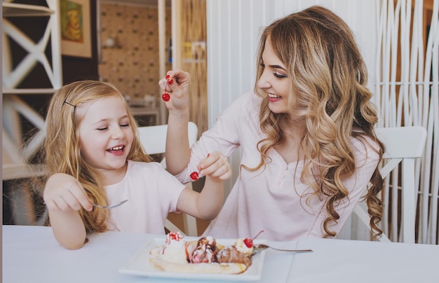 Meisje met moeder en elkaar kersen ijs voeden in een gezellig café. Goede relatie tussen ouders en kind.