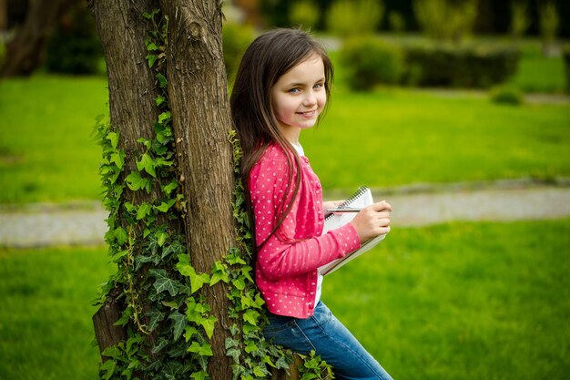 Meisje met notitieboekje en pen dichtbij boom