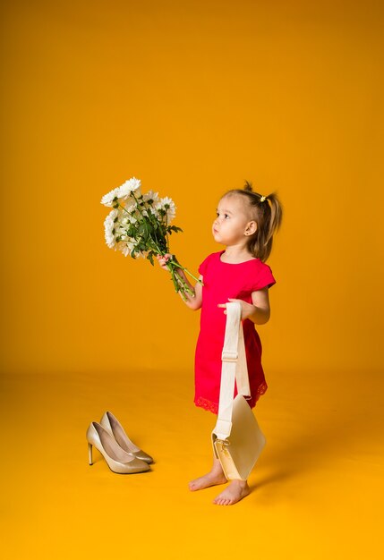 Meisje met paardenstaarten in een rode jurk staat zijwaarts met een boeket witte bloemen op een gele ondergrond met ruimte voor tekst