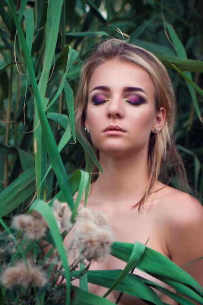 Meisje met paarse smokey make-up poseren tegen een achtergrond van groene struiken