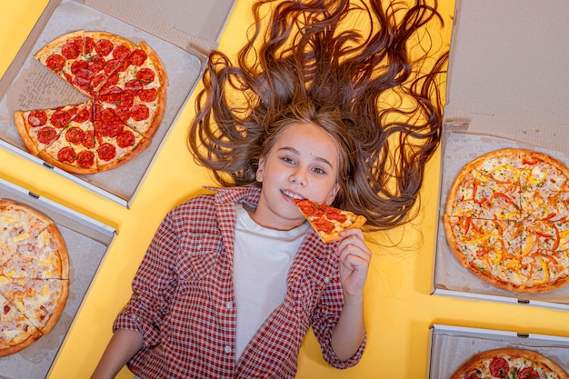 Foto meisje met pizza ligt op een gele achtergrond