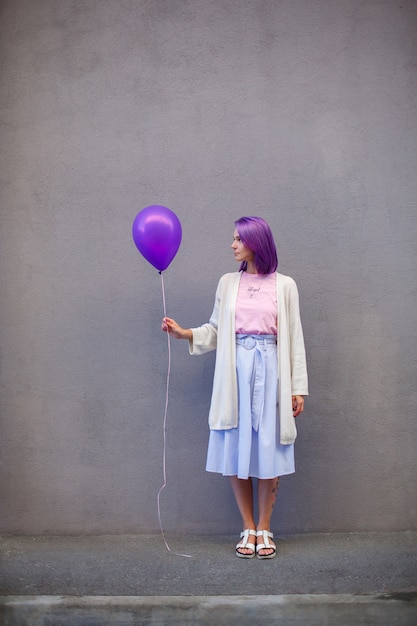 Meisje met purper haar dat zich voor grijze muur en greep airballoon bevindt