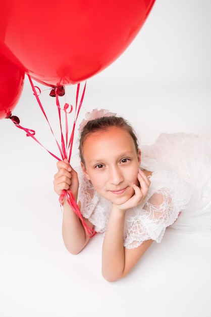 Meisje met rode ballonnen in de hand en positief kijken naar camera liggend op witte achtergrond