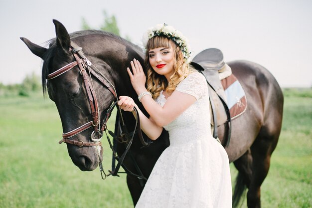 Meisje met rode lippen in een witte jurk bij een zwart paard