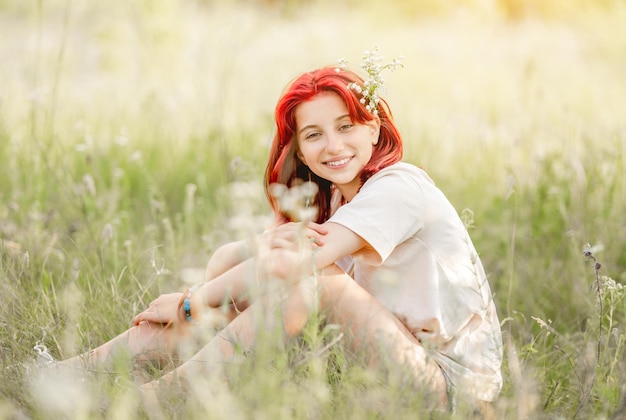 Meisje met rood haar dat in de natuur zit en lacht Mooie jonge vrouw in het zonnige veld met bloemen