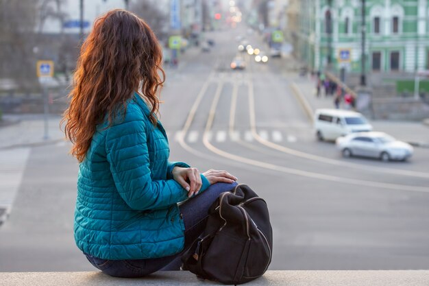 Meisje met rood haar kijkt naar de avondstraat in de stad