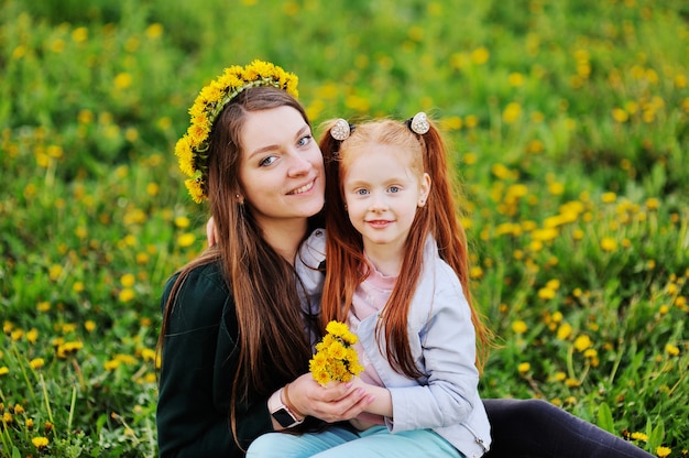 Meisje met rood haar knuffels haar moeder op de achtergrond van een veld met paardebloemen