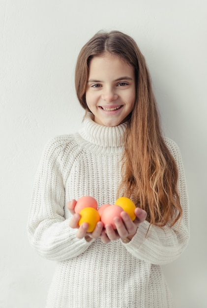 Foto meisje met roze en gele paaseieren in haar handen, die een witte sweater draagt