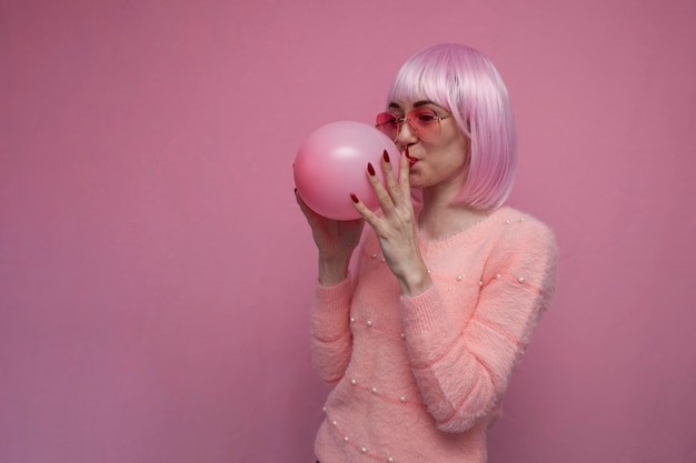 Meisje met roze haar blaast een roze ballon op een roze achtergrond op