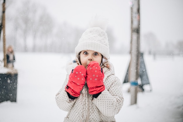 Meisje met roze sneeuwhandschoenen staat buiten op een sneeuwdag.