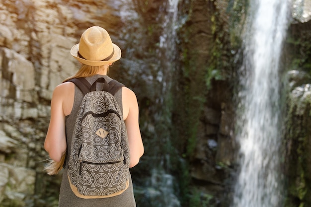 Meisje met rugzak en in een hoed die een waterval bekijkt. Uitzicht vanaf de achterkant