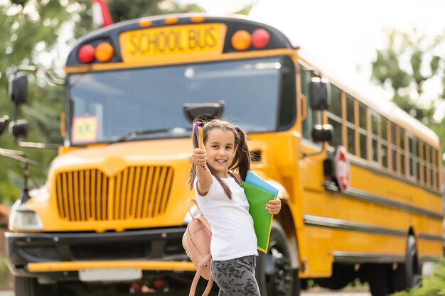 Meisje met rugzak in de buurt van gele schoolbus. Vervoer voor studenten