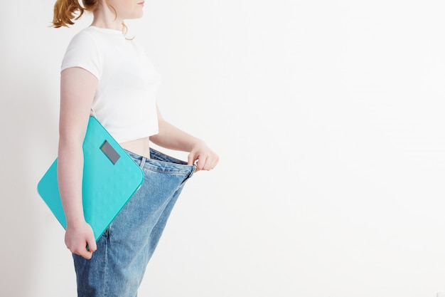 Meisje met schaal die haar grote jeans trekt en gewichtsverlies toont