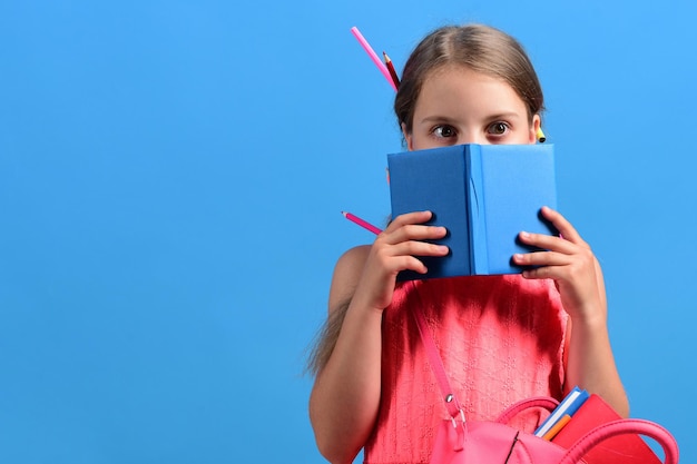 Meisje met schooltas verstopt zich achter blauw notitieboekje