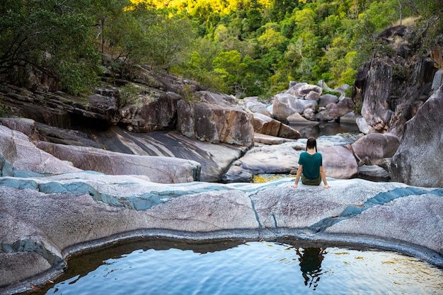 meisje met staartjes zit op kleurrijke rotsen bij jourama watervallen bij zonsondergang, queensland, australië