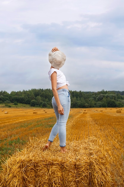 Meisje met strohoed staat op een hooiberg op een baal