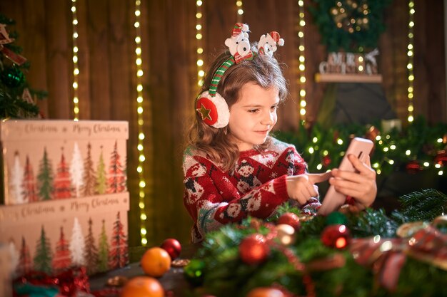 Meisje met telefoon in de buurt van de kerstboom in het decoratieve interieur.