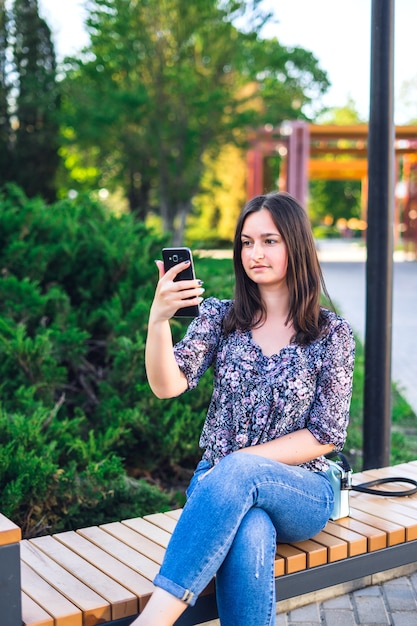 Meisje met telefoonzitting op bank in park.