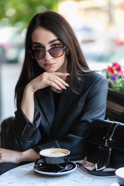 Meisje met zonnebril zittend in een café, coffeeshop, zittend op een stoel in de stad met rode bloemen, zonnebril dragend