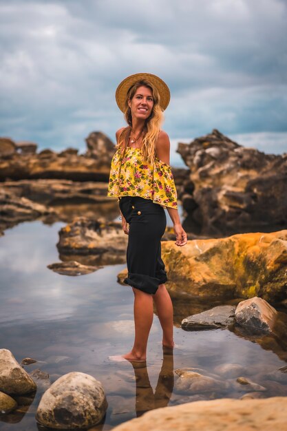 MEISJE MET Zwarte korte broek en strohoed in een natuurlijk landschap aan zee bij zonsondergang