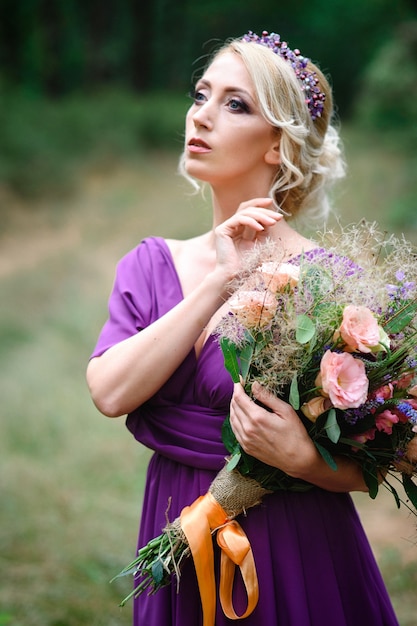 Meisje model blond in een lila jurk met een boeket met een groen bos