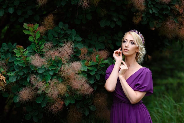 Meisje model blond in een lila jurk met een boeket met een groen bos
