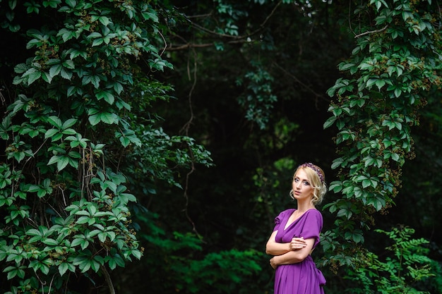 Meisje model blond in een lila jurk met een boeket met een groen bos