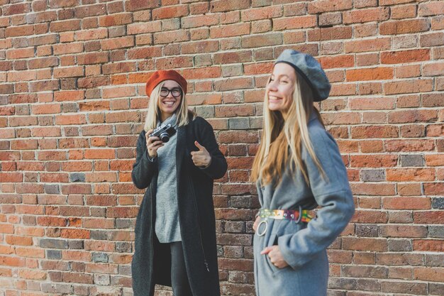 Meisje neemt foto van haar vriendin voor bakstenen muur in stedelijke straatfotograaf en yout