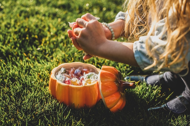 Meisje neemt snoepjes. op groen gras oranje keramische pompoen met halloween-snoepjes. portemonnee of leven. herfsttradities