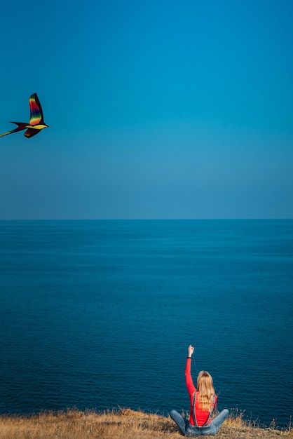 Meisje op een berghelling aan zee lanceert een vlieger op een zonnige dag