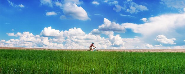 Meisje op een fiets in een groen gebied tegen mooie blauwe hemel met witte wolken. Panorama. Landschap. Vrijheid concept.