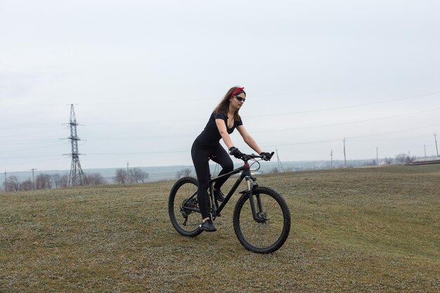 Meisje op een mountainbike op offroad mooi portret van een fietser in regenachtig weer Fitness meisje rijdt op een moderne koolstofvezel bergfiets in sportkleding Closeup portret van een meisje in rode bandana