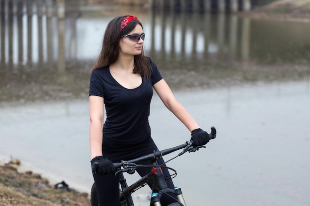 Meisje op een mountainbike op offroad mooi portret van een fietser in regenachtig weer Fitness meisje rijdt op een moderne koolstofvezel mountainbike in sportkleding Close-up portret van een meisje in rode bandana